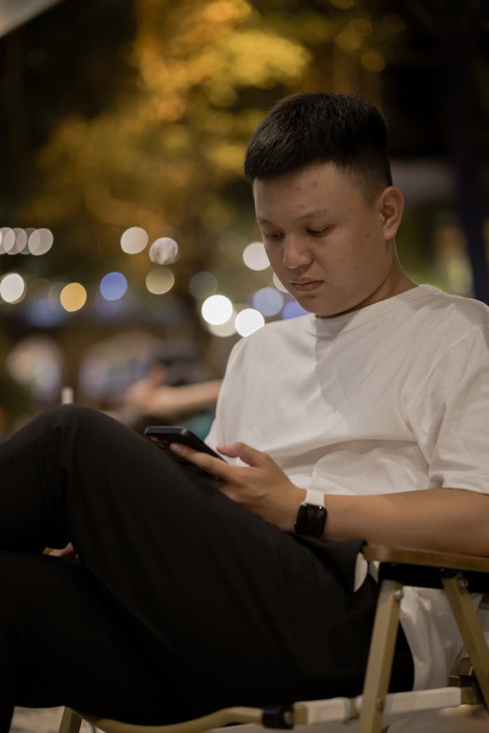 Young man in white t-shirt using smartphone outdoors at night.