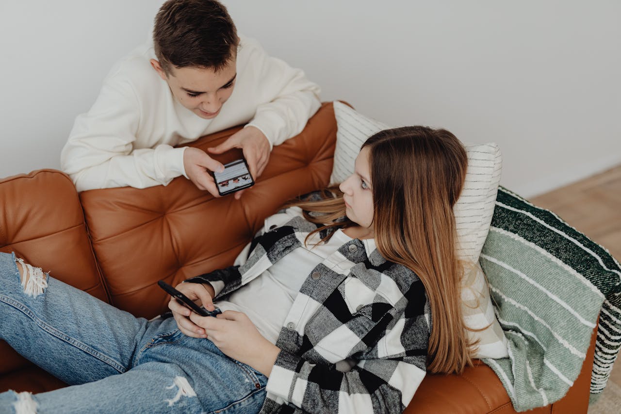 Two teenagers lounging on a sofa, engaging with smartphones. Perfect for lifestyle and technology themes.